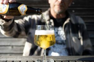 Adult pouring beer into a glass outside on a sunny day, featuring a clear, refreshing drink.